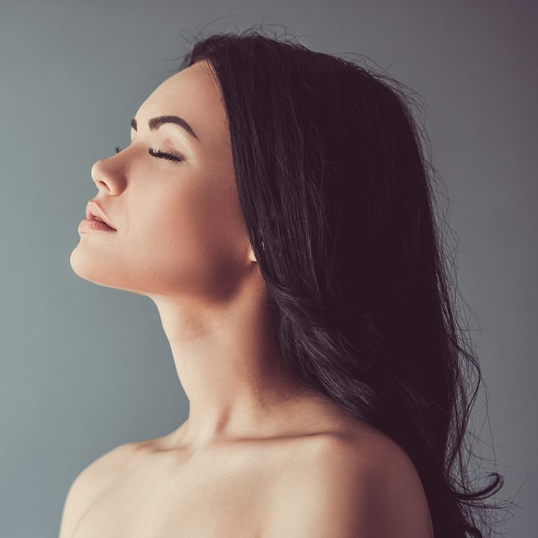 Profile of beautiful young brunette with bare shoulders and closed eyes, on gray background