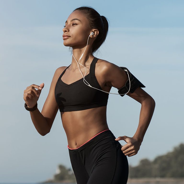 Side view shot of young woman in sportswear jogging on beach. African-american female jogger runner running outdoors. Active lifestyle concept